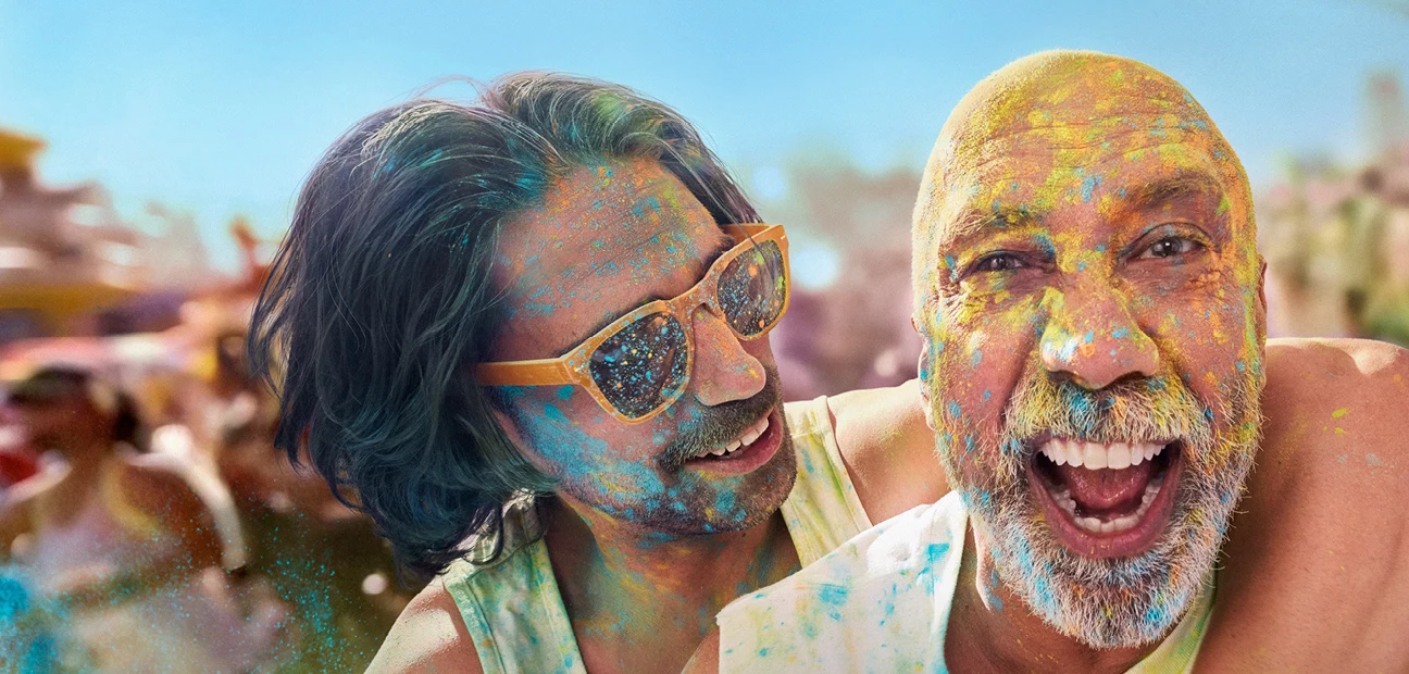Worth Doing Well visual: two men covered in coloured powder at a colour run, mid laugh