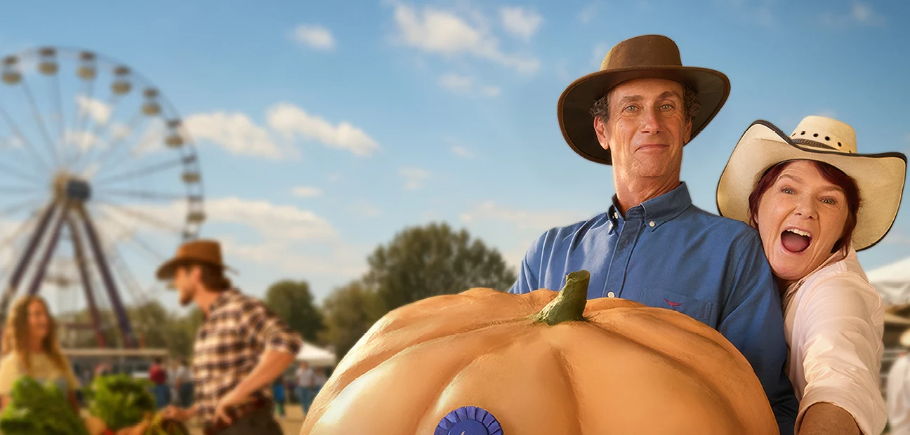Worth Doing Well visual: a couple holding a prize pumpkin at a country show, with a Ferris wheel and market stalls behind them