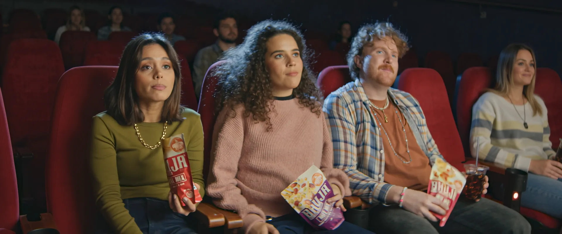 Three friends in red cinema seats with Bhuja, in a full cinema built around them
