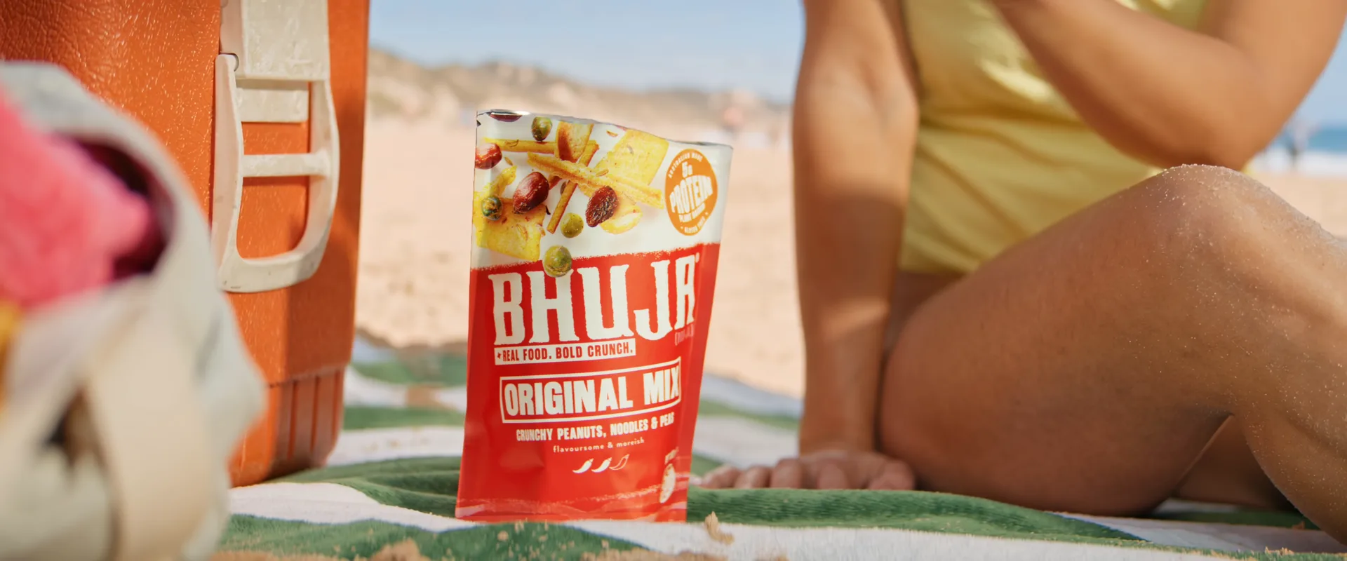 A Bhuja Original Mix pack on a beach towel beside an esky, from the Bhuja relaunch TVC