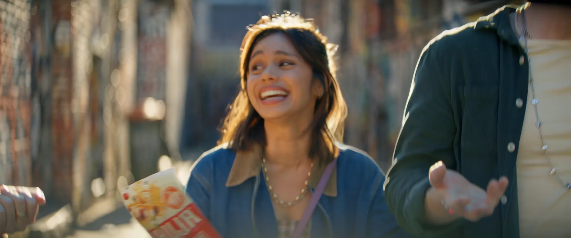 A woman laughing with a Bhuja pack in a sunlit city laneway