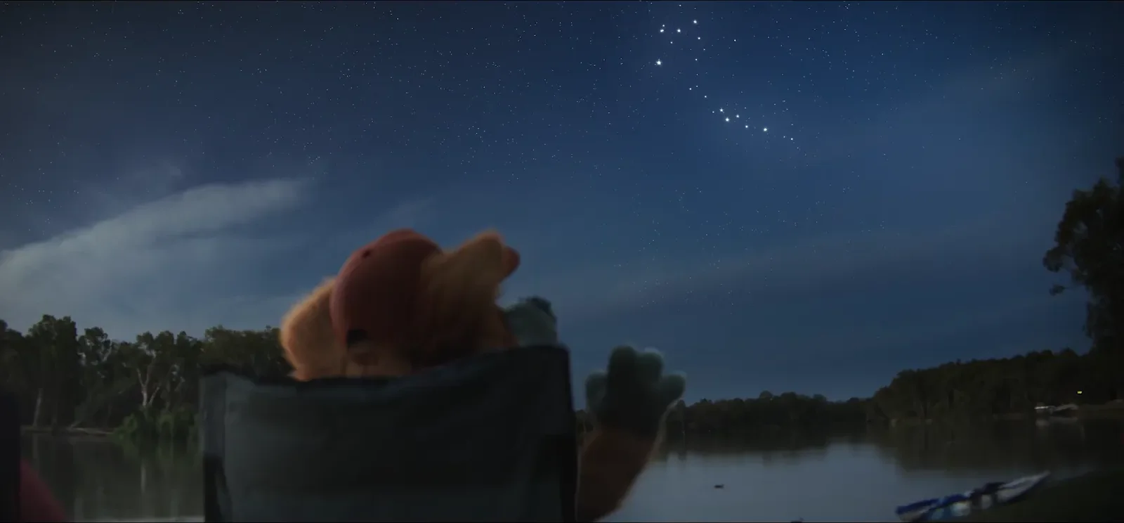 Bruce sitting in a camp chair beside a river under a night sky