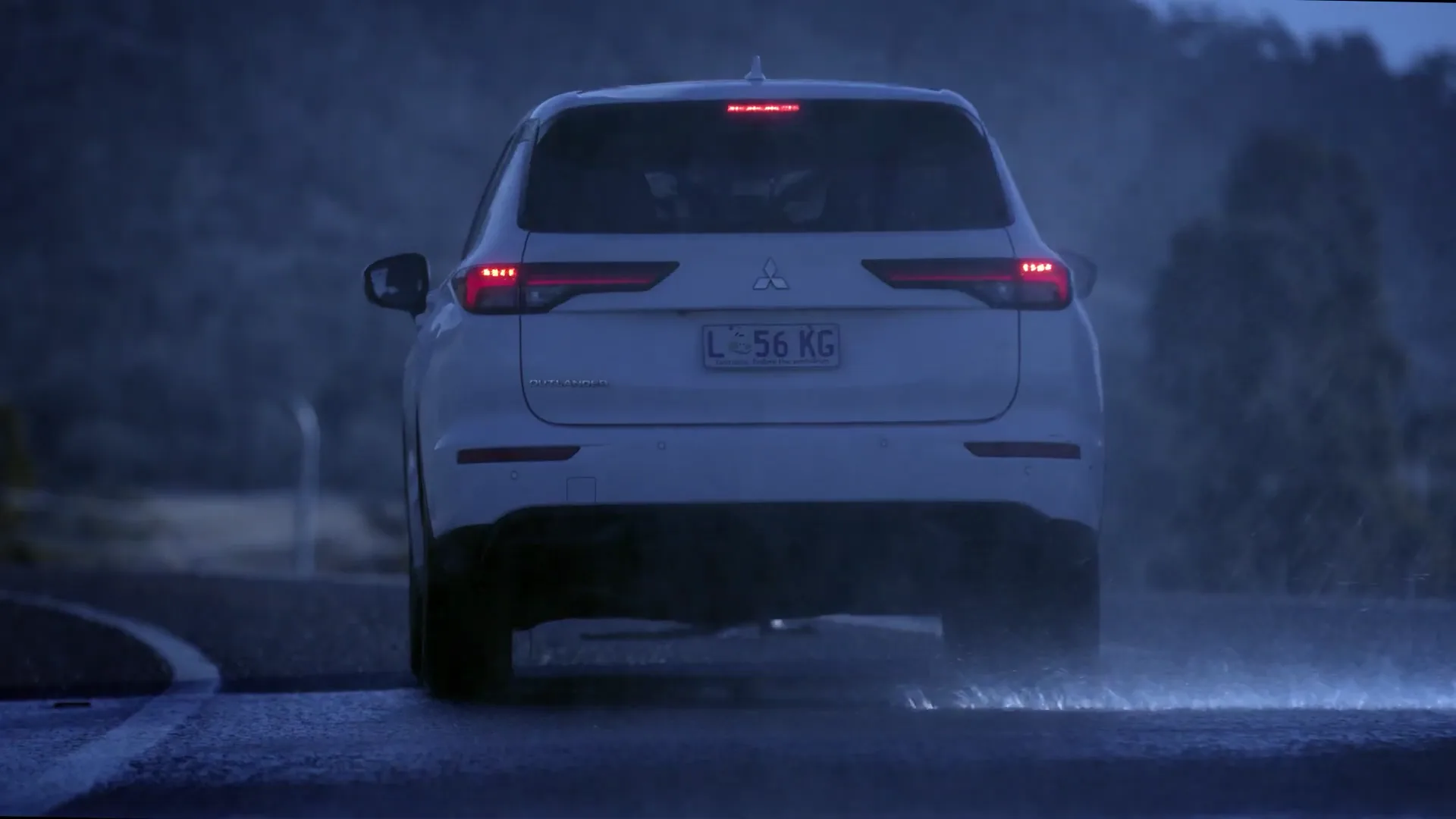 The same white SUV from behind on a wet road at night, brake lights on and spray rising from the tyres